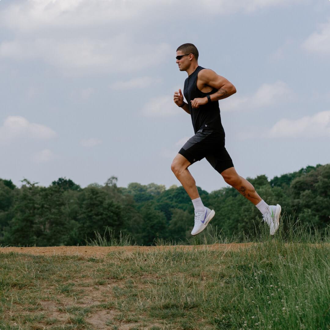 A man running through a grassy field with a treeline in the background