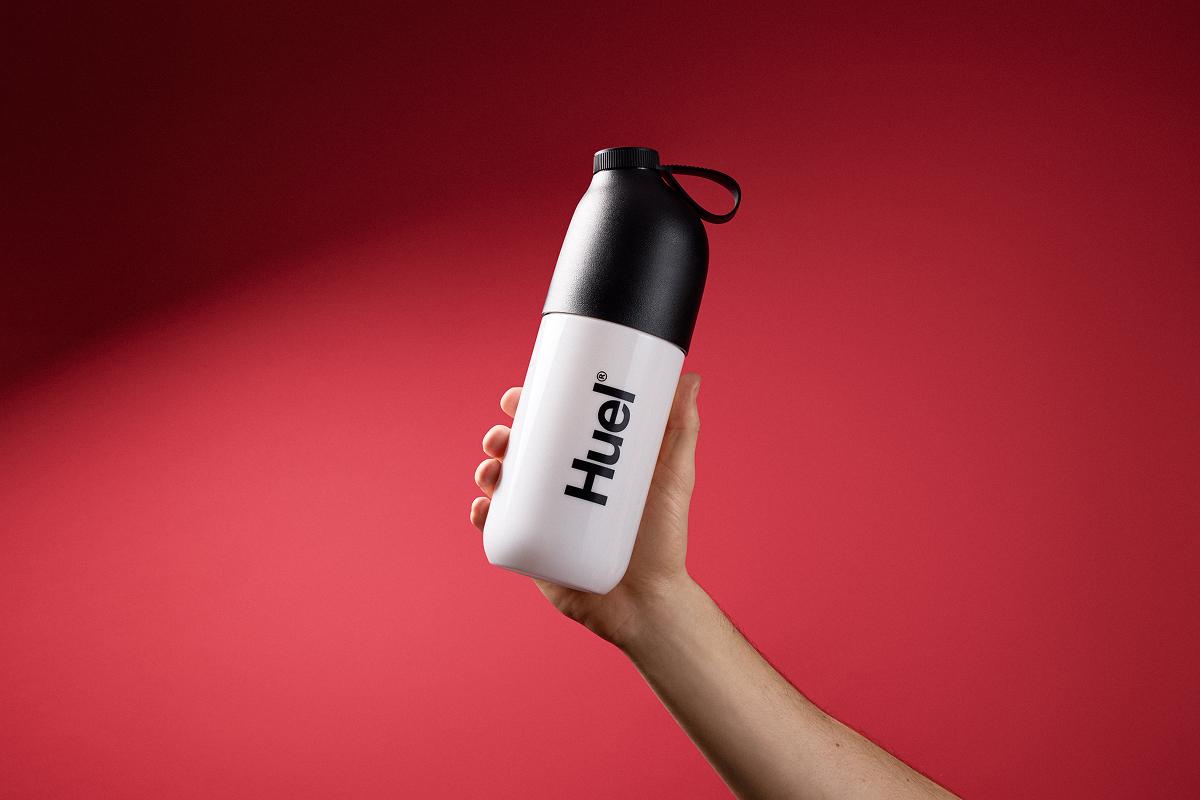Person holding a Huel Shaker on red background