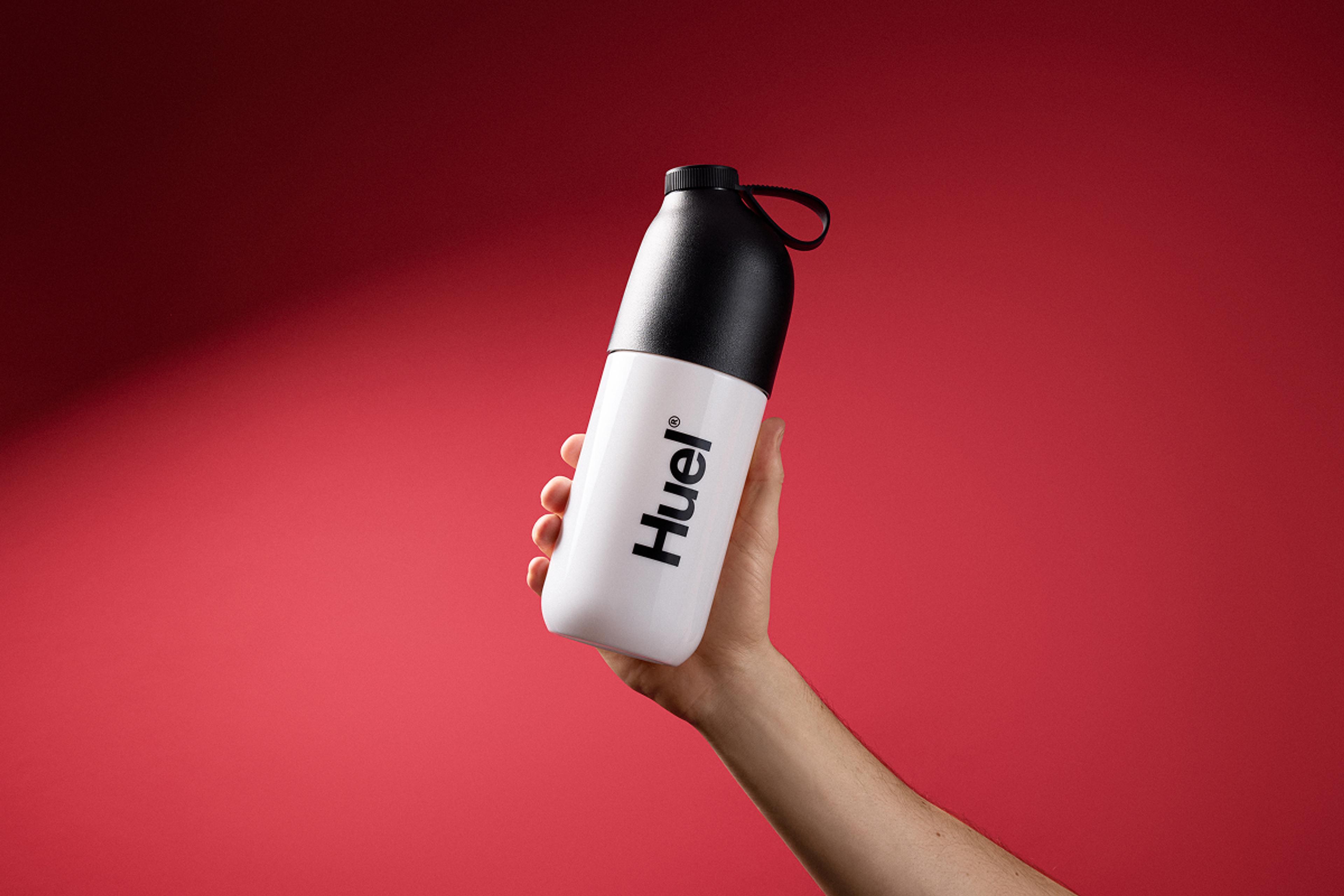 Person holding a Huel Shaker on red background