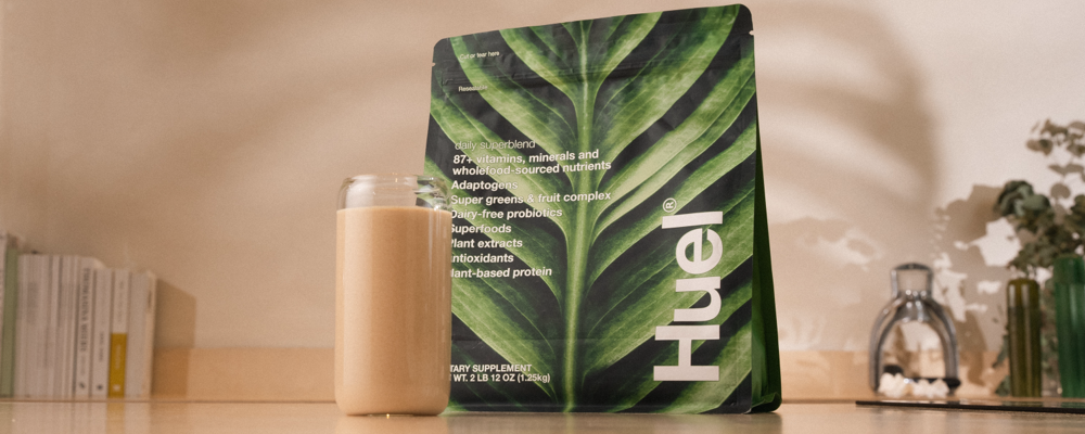 Green Huel Superblend pouch on a counter with a glass of Superblend beside it