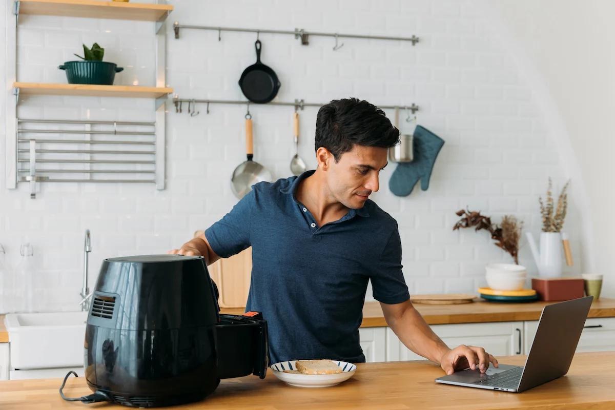 man using his laptop and air fryer in the kitchen