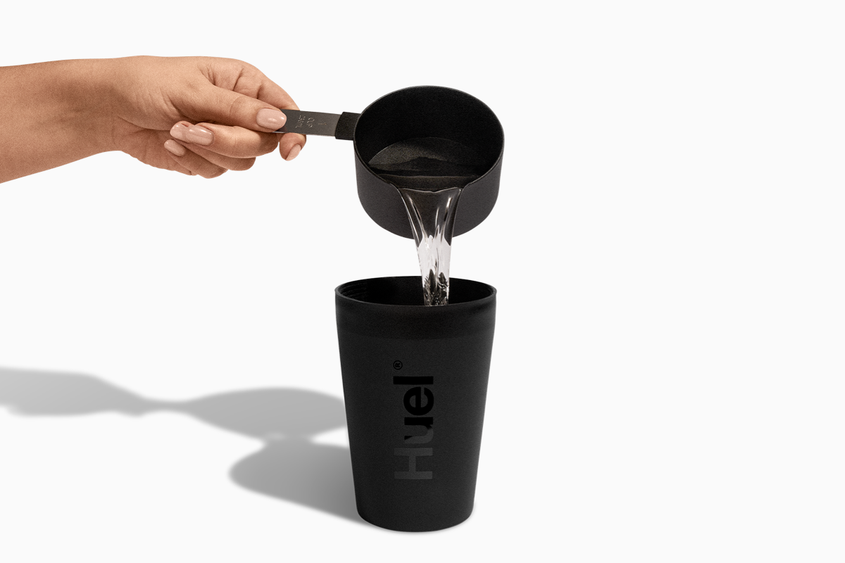 Image of someone pouring water from a black Huel scoop into a Huel pot
