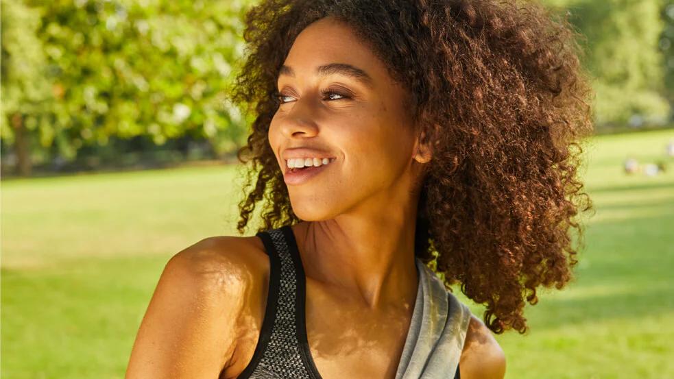 woman outside in a field smiling with trees in the background