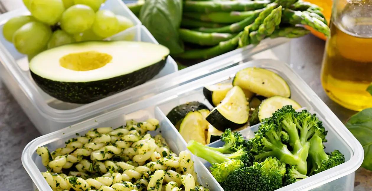 a vibrant mix of green fruits vegetables and pesto pasta in plastic meal prep containers