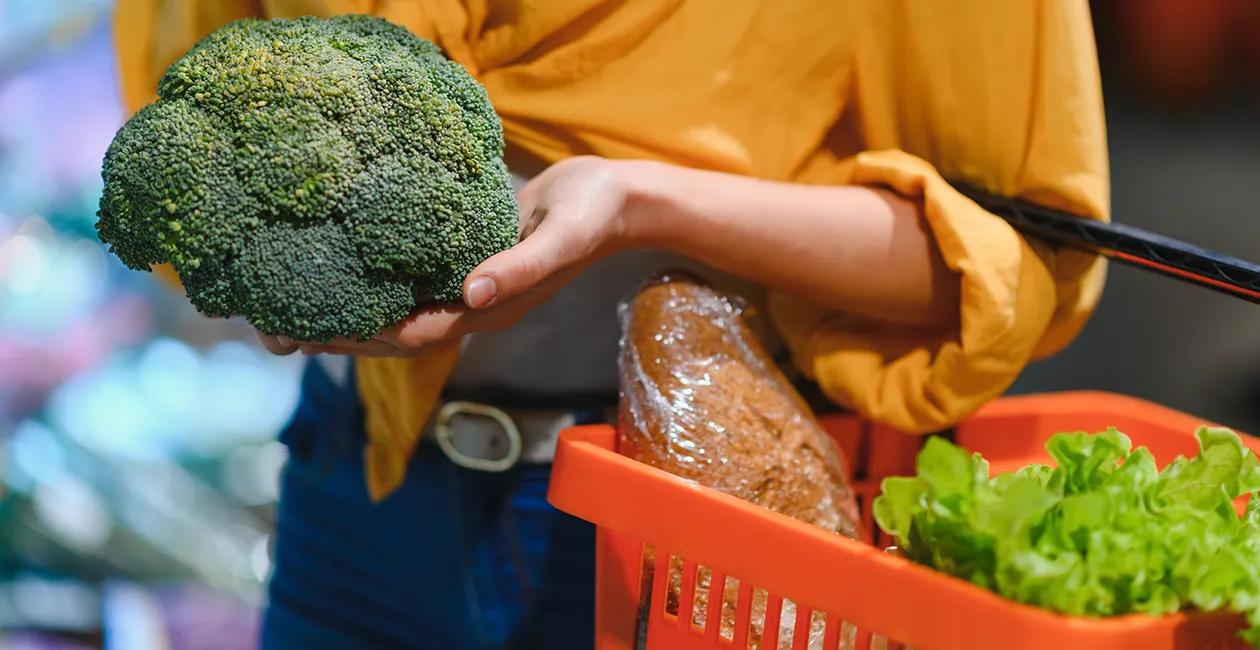 woman shopping holding a broccoli in her hands and a basket with organic produce