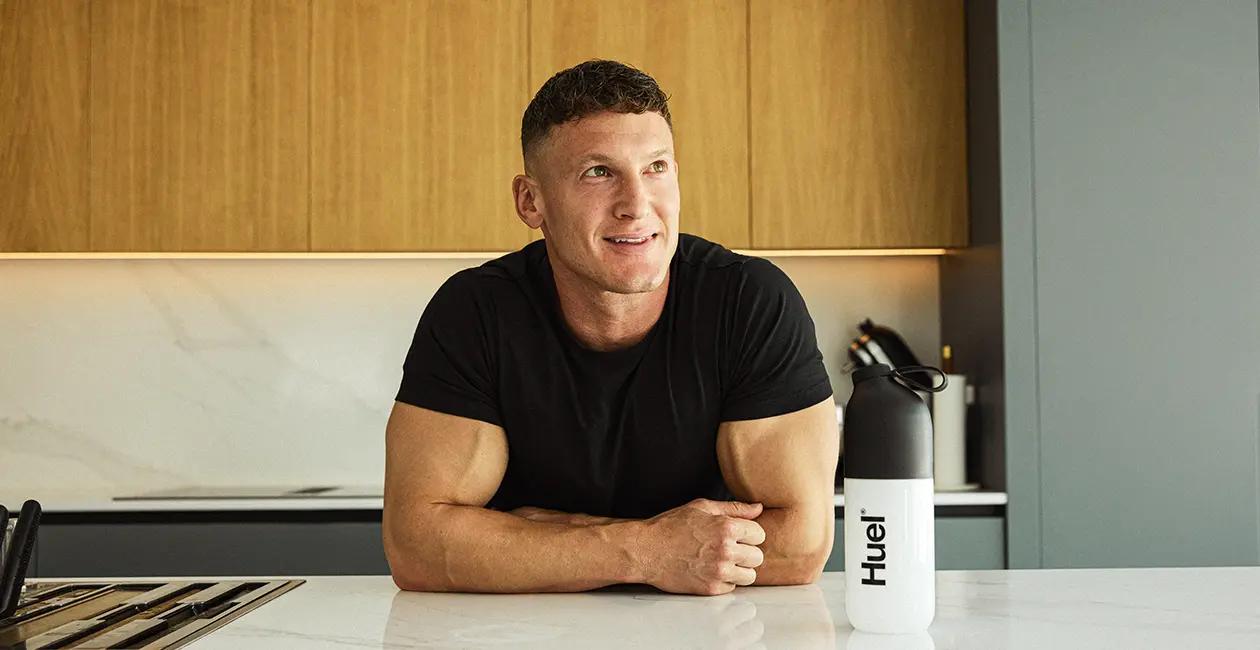 Matt Morsia leaning on a kitchen counter with a Huel shaker next to him