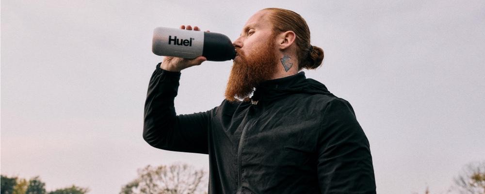 Man taking a break from running while drinking Huel Complete Protein powder shake from a Huel Shaker