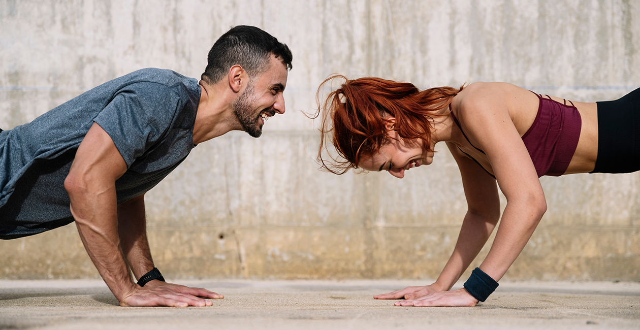 A man and woman smiling while doing press ups