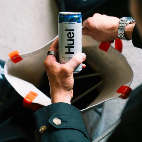A man sitting on a wooden park bench placing a huel daily a-z vitamins drink can down next to him