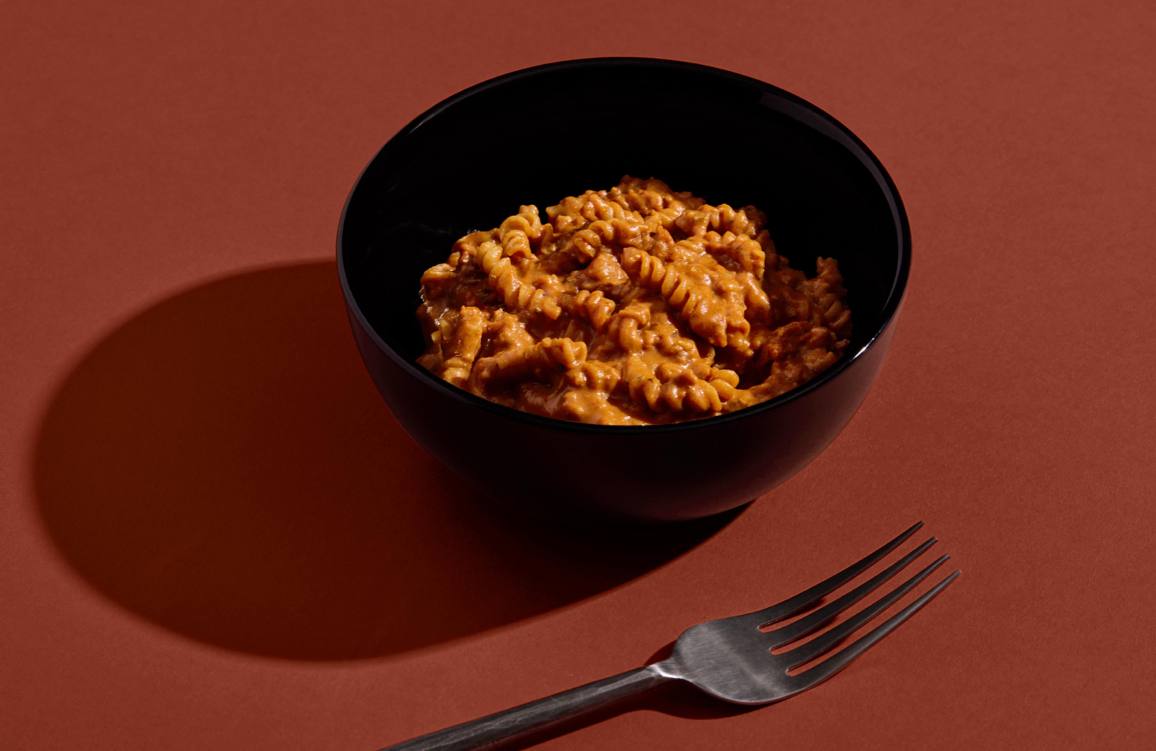 Close-up of H&S Bolognese Bowl set against a red background next to a metal fork