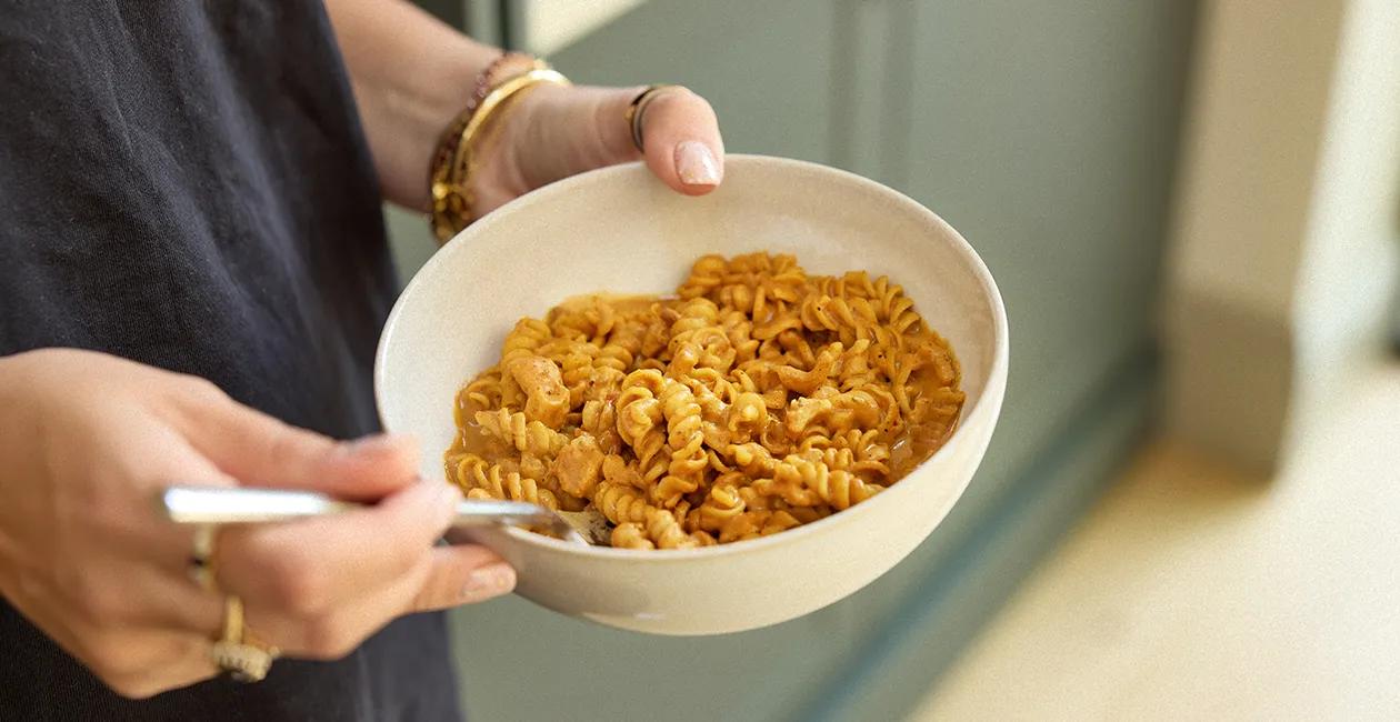 close up of a person holding a bowl of Huel Hot & Savoury pasta in a bowl with a fork