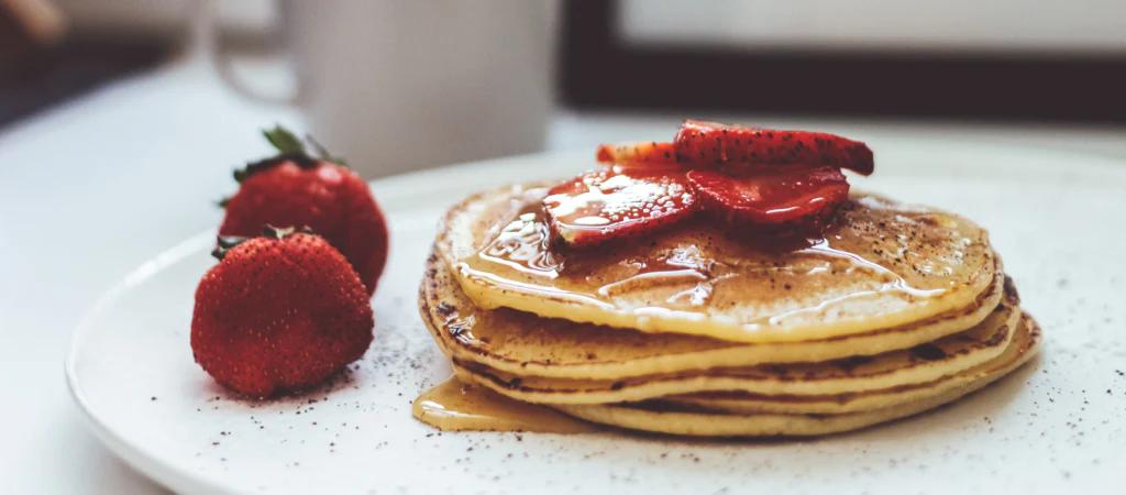 banana and strawberry pancakes on a white plate garnished with whole strawberries on the side