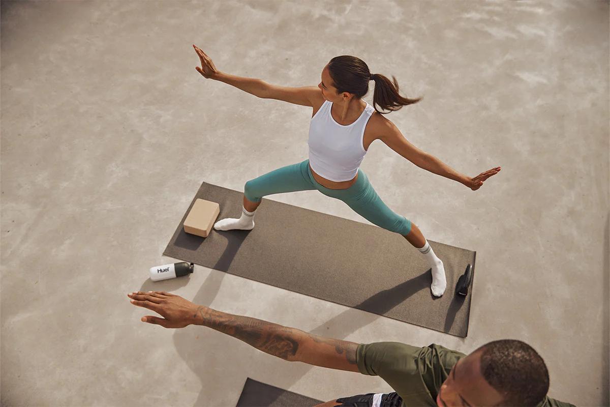 two people on yoga mats doing yoga poses with a kettlebell and huel shaker on the floor next to them