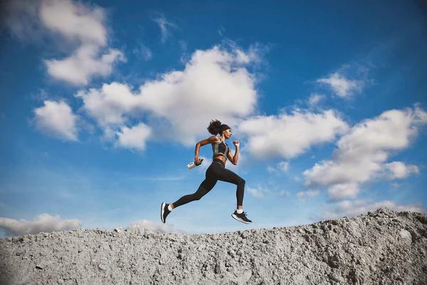 Woman running on top of a mountain holding a Huel shaker and with clouds in the background