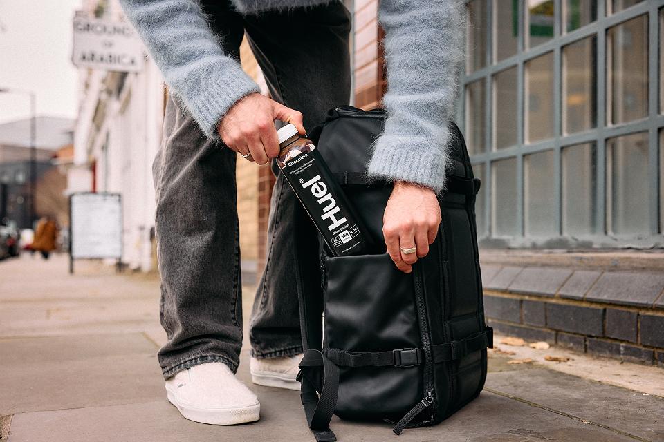 Man putting Huel Black Edition ready-to-drink in a black backpack