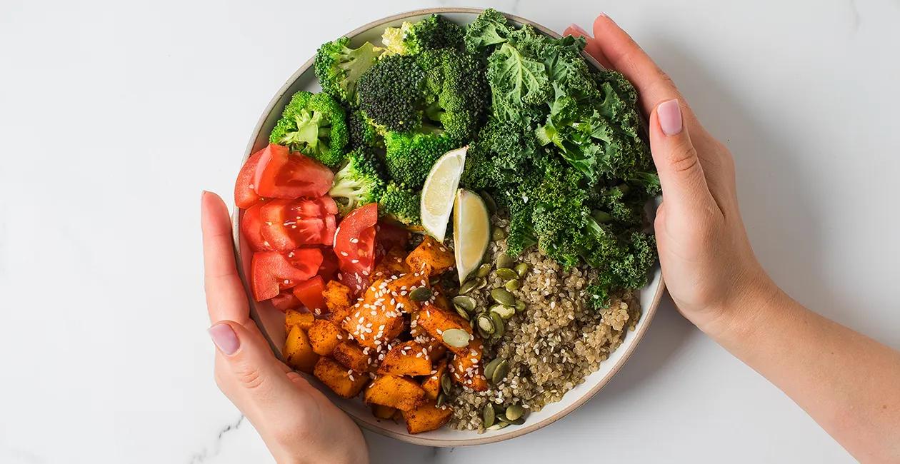 A bowl of healthy food with a persons hands either side of the white bowl