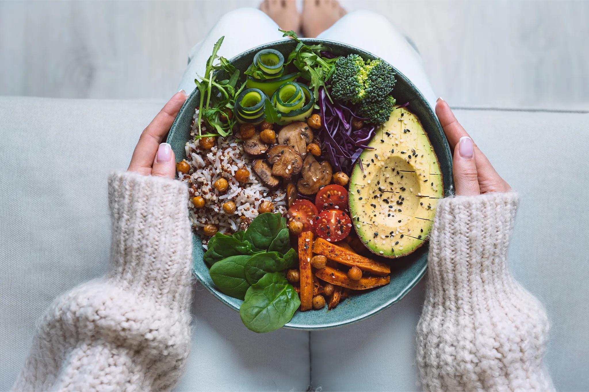person holding a bowl with avocado cucumber tomato carrot spinach broccili mushrooms and rice on their lap