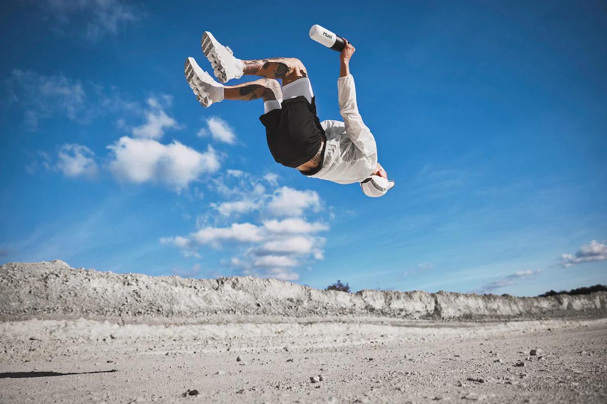 Man doing a backflip outside whilst holding a Huel shaker