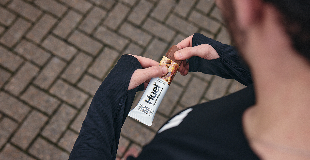 man stood outside opening a Huel Complete Nutrition Bar