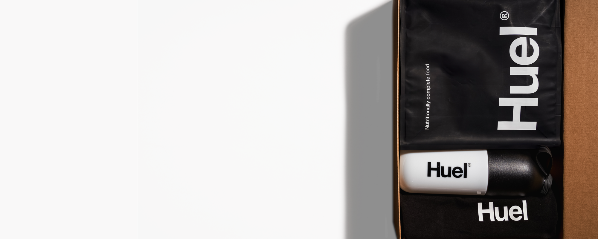 Das Auspacken einer Huel-Lieferung – die braune Box enthält mehrere Huel Pulver, Protein-Drinks und Protein-Snacks.