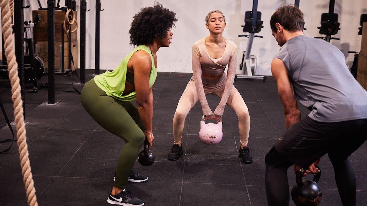 three people at the gym doing kettlebell squats