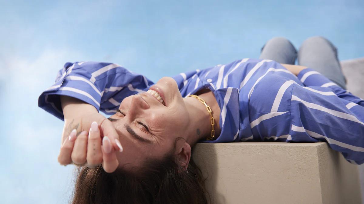 Woman in a purple and white striped shirt laying on a wall with her head hanging over the edge