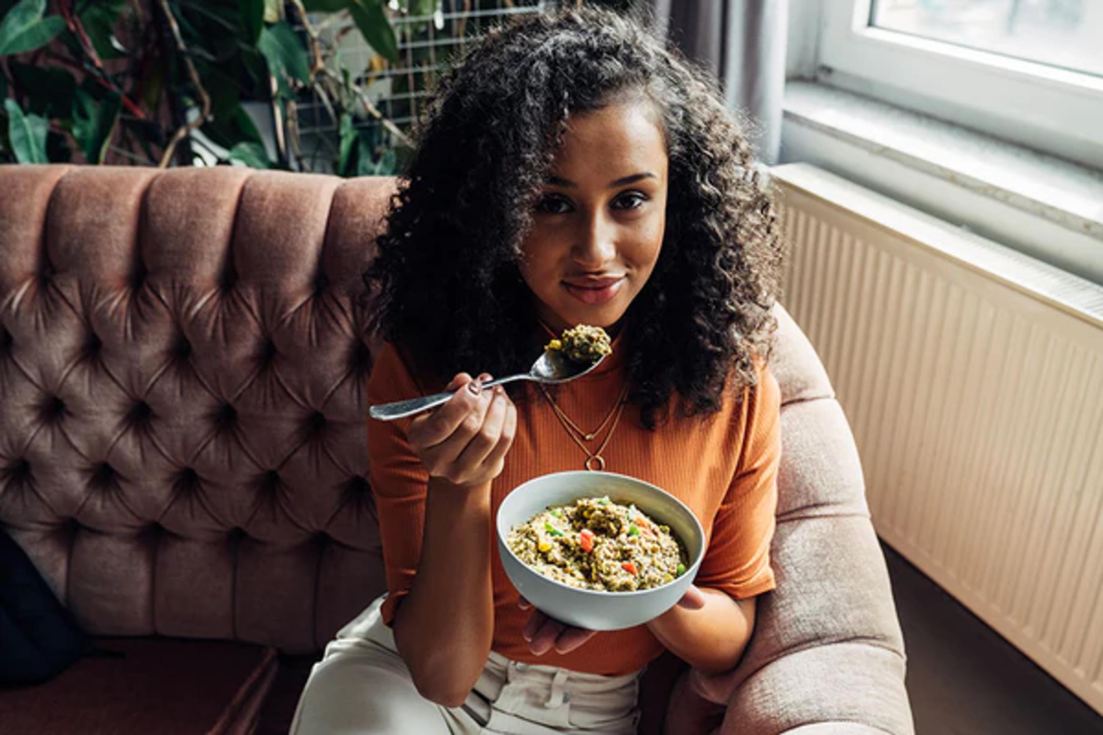 woman sat on a sofa eating from a bowl looking at the camera