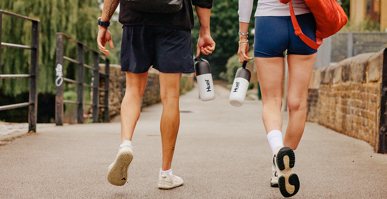 A man and woman walking away both holding Huel shakers