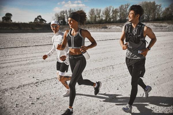 Three people running on a dirt track holding Huel products and smiling