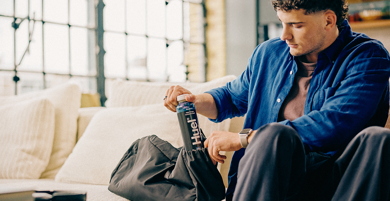 A man sat on a couch wearing a blue shirt putting a Black Edition Ready-to-drink in his bag