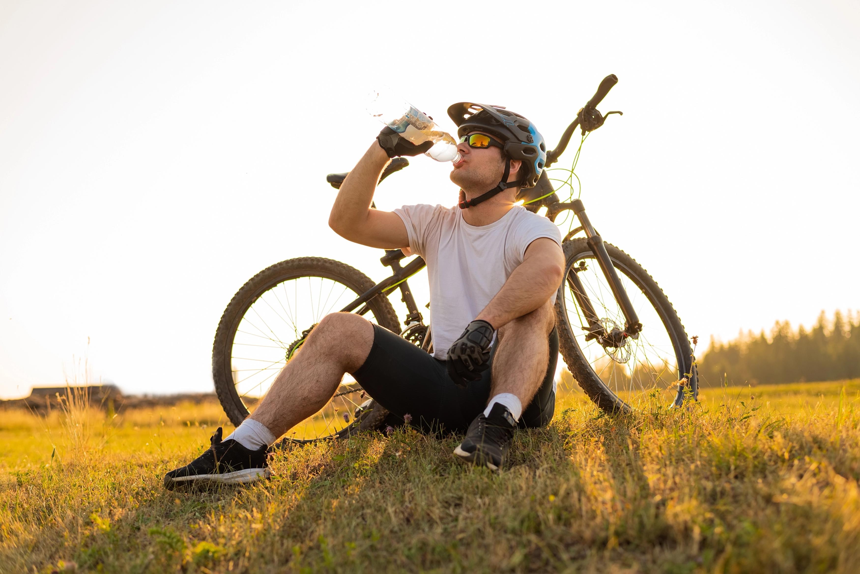 man sat on the grass drinking from his water bottle with his bicycle behind him