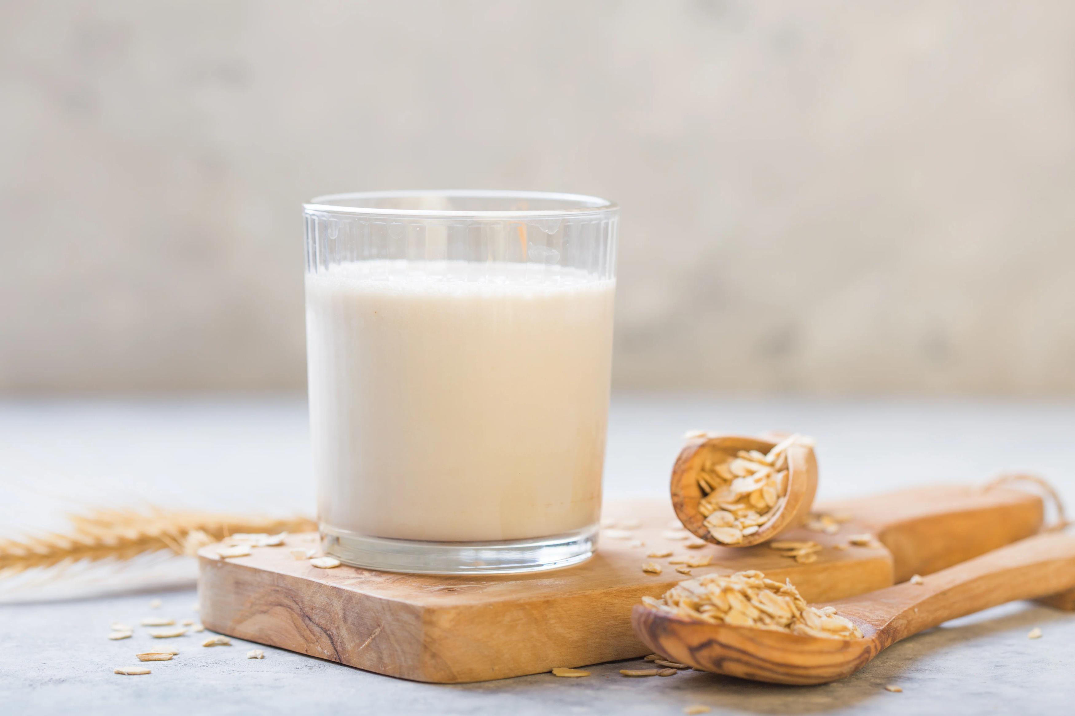 milk in a glass on a wooden board with a wooden spoon full of oats next to it