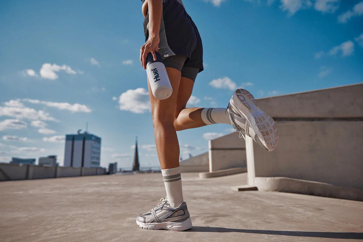 person wearing atheltic gear walking on concrete outside holding a Huel shaker