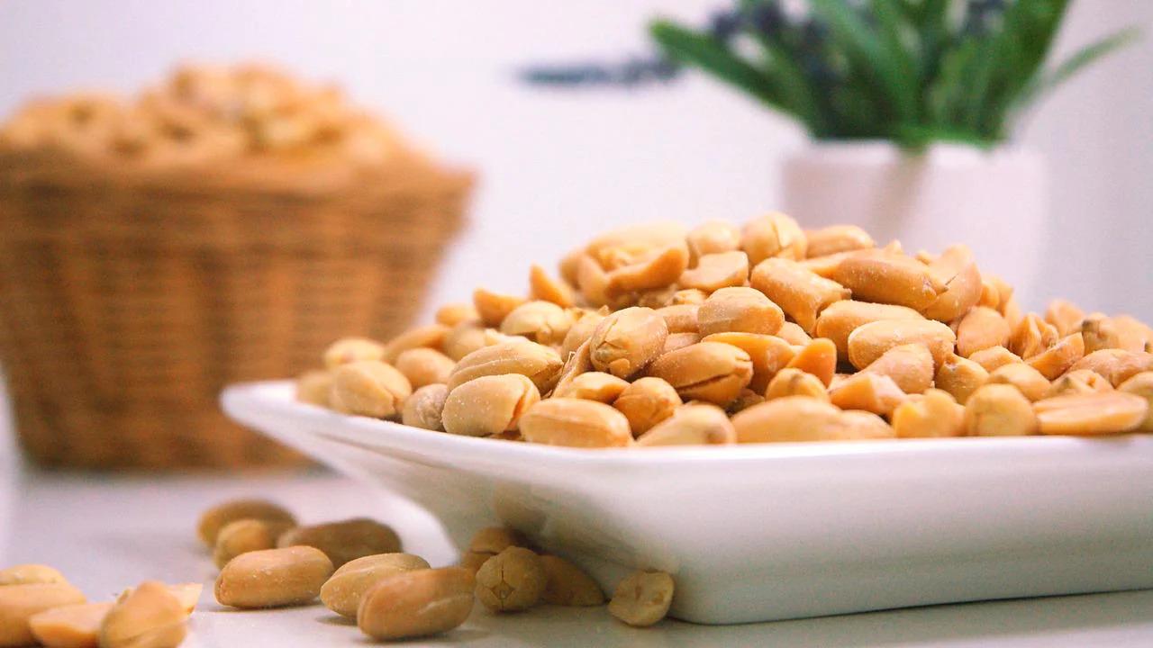 Plate of peanuts with a wicker basket of peanuts in the background
