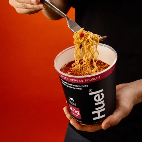 A man pulling a forkful of spicy korean noodles on an orange red gradient background