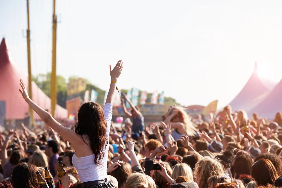 Woman with her arms stretched out, sat on someone's shoulders in a crowd at a festival