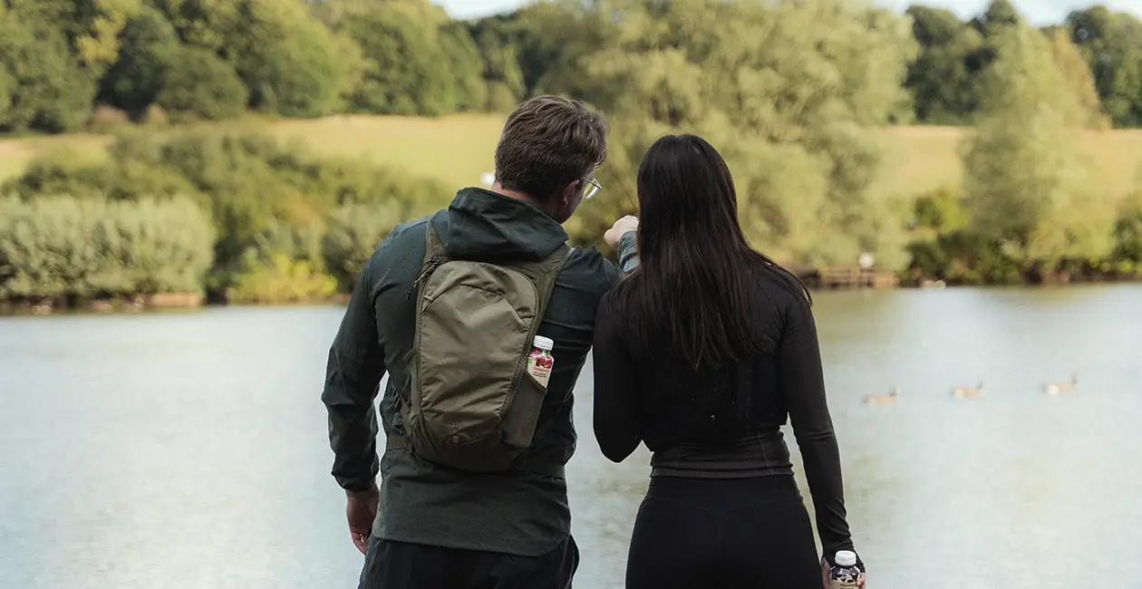 man and woman stood looking over a lake with their back to the camera and a Huel Lite Ready-to-drink in the pocket of the mans backpack
