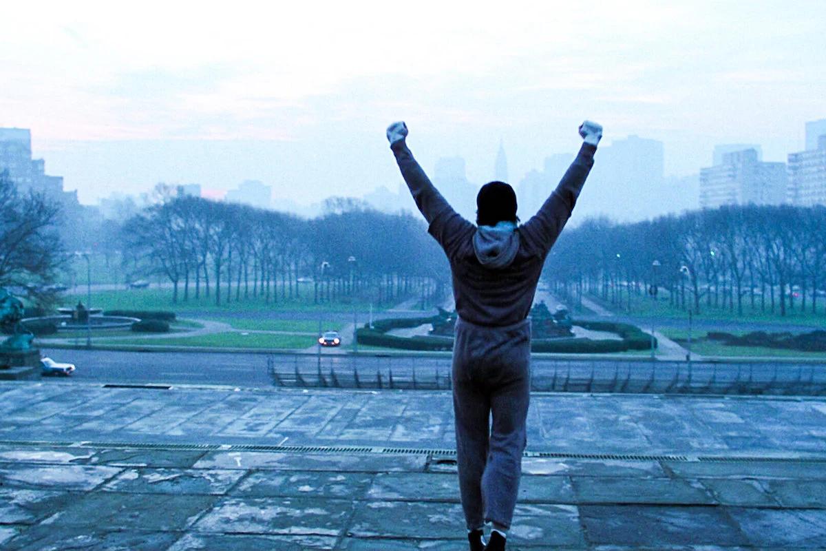picture from behind of Rocky standing with his arms in the air on a foggy morning