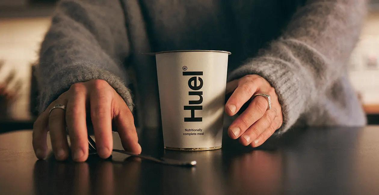 person at a table reaching for a fork with a Huel Hot and Savoury in front of them