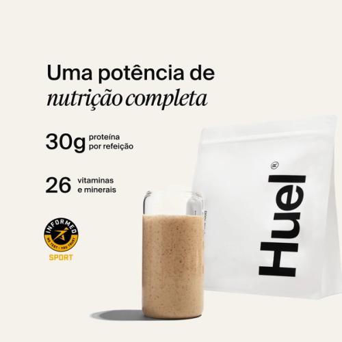 A bag of Huel powder next to a glass containing a Huel drink on a neutral background
