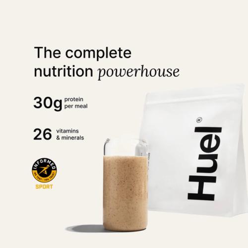 A bag of Huel powder next to a glass containing a Huel drink on a neutral background