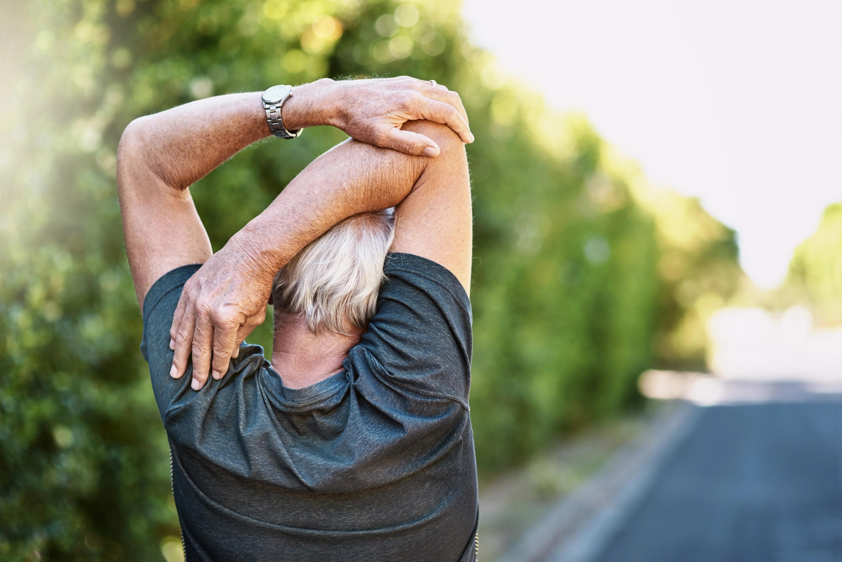man outside stretching his arm behind his back
