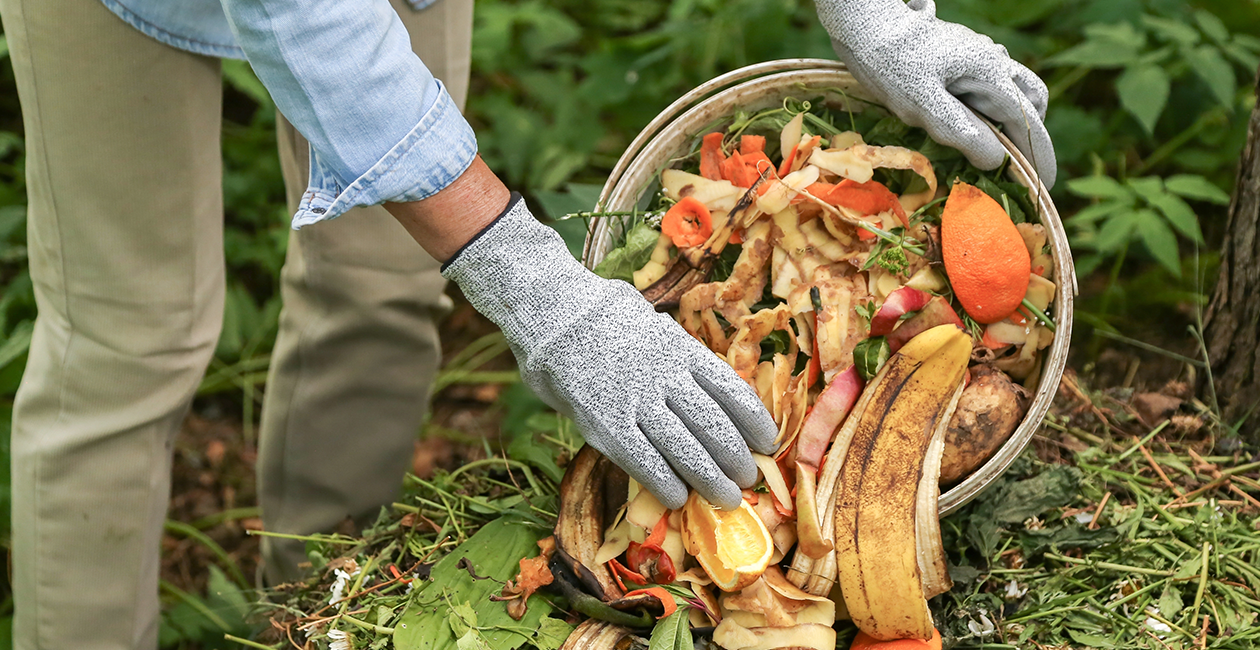 person adding food waste to a compost heap in a garden