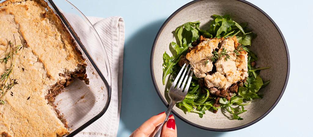vegan sheperds pie in a glass dish on the left and a serving on a bed of leafy greens in a bowl on the right