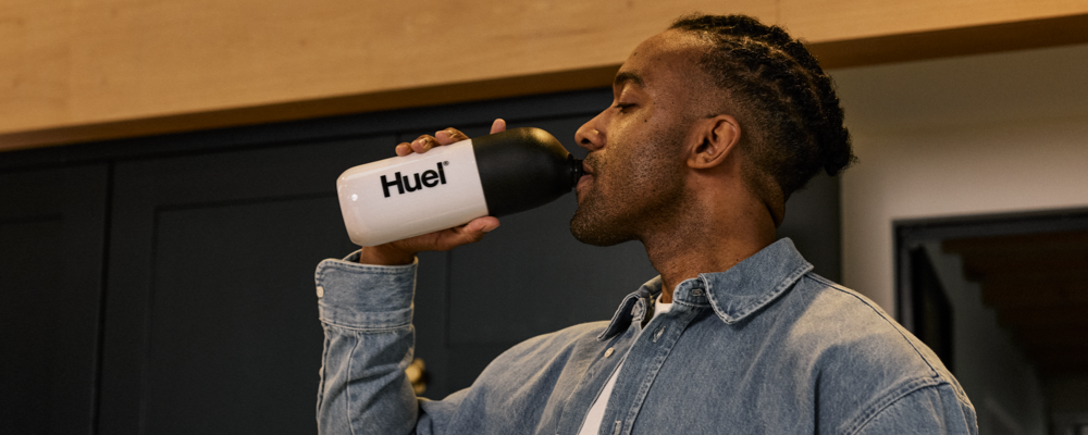 Side view of a man drinking from a black and white Huel shaker bottle