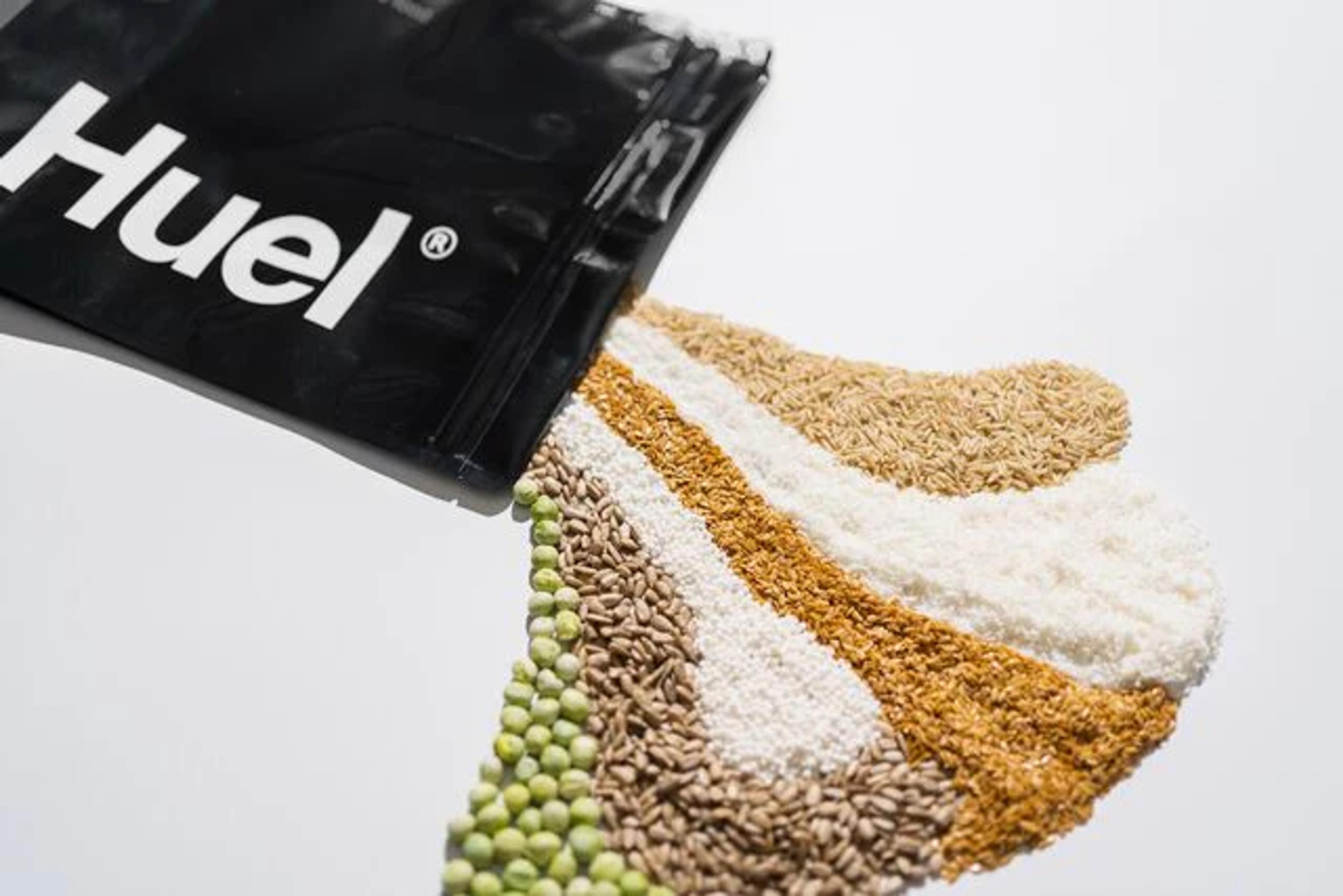 a bag of huel black edition lying flat with a variety of seeds and grains spilling out