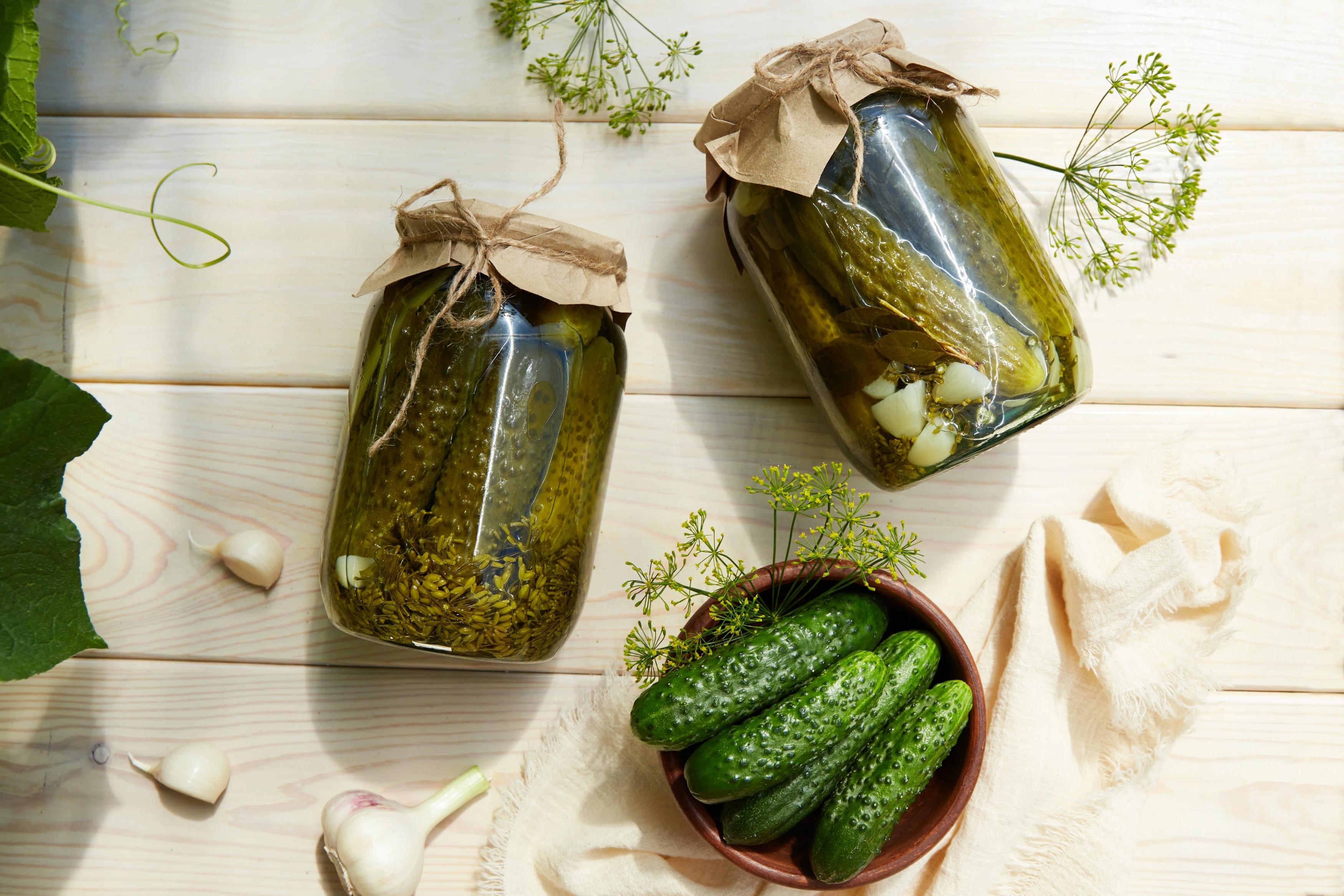 two jars on their side filled with pickles and garlic next to a bowl of pickles