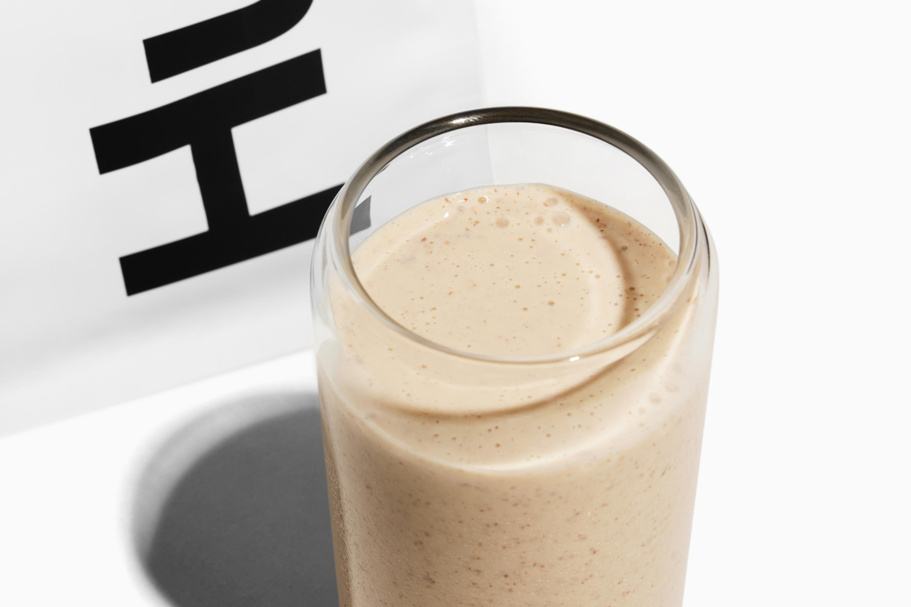 Huel パウダーの白い袋の横に置かれた、Huel シェイカーのグラス