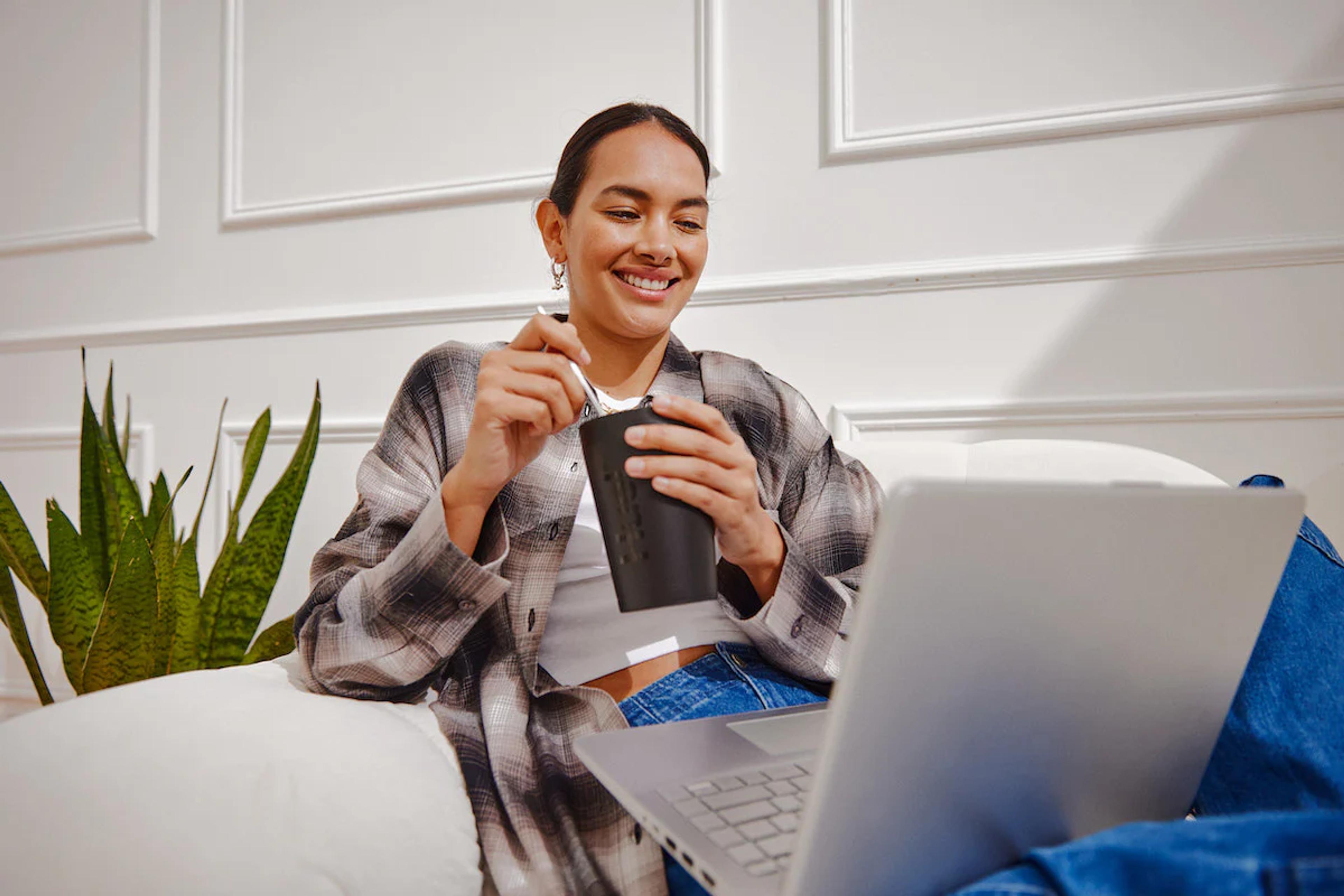 woman sat on a sofa eating huel hot and savoury while watching her laptop