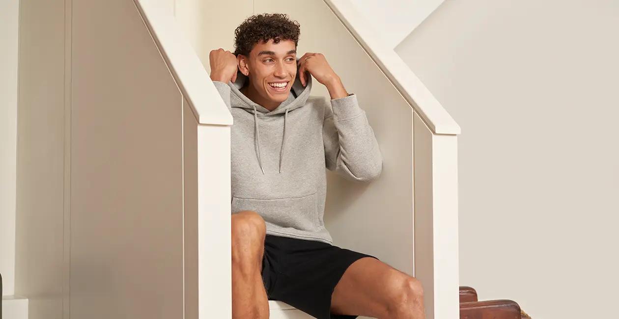 man sat on stairs smiling pulling up the hood on his hoodie